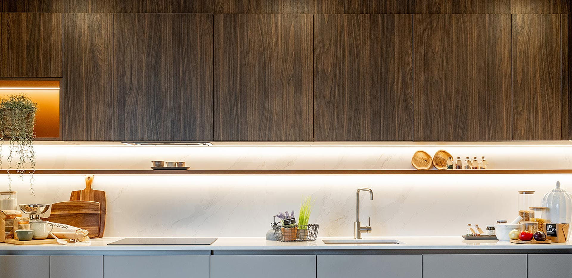 Kitchen with grey matte and wood pattern cupboards, modern appliances, chrome taps, strip lighting.