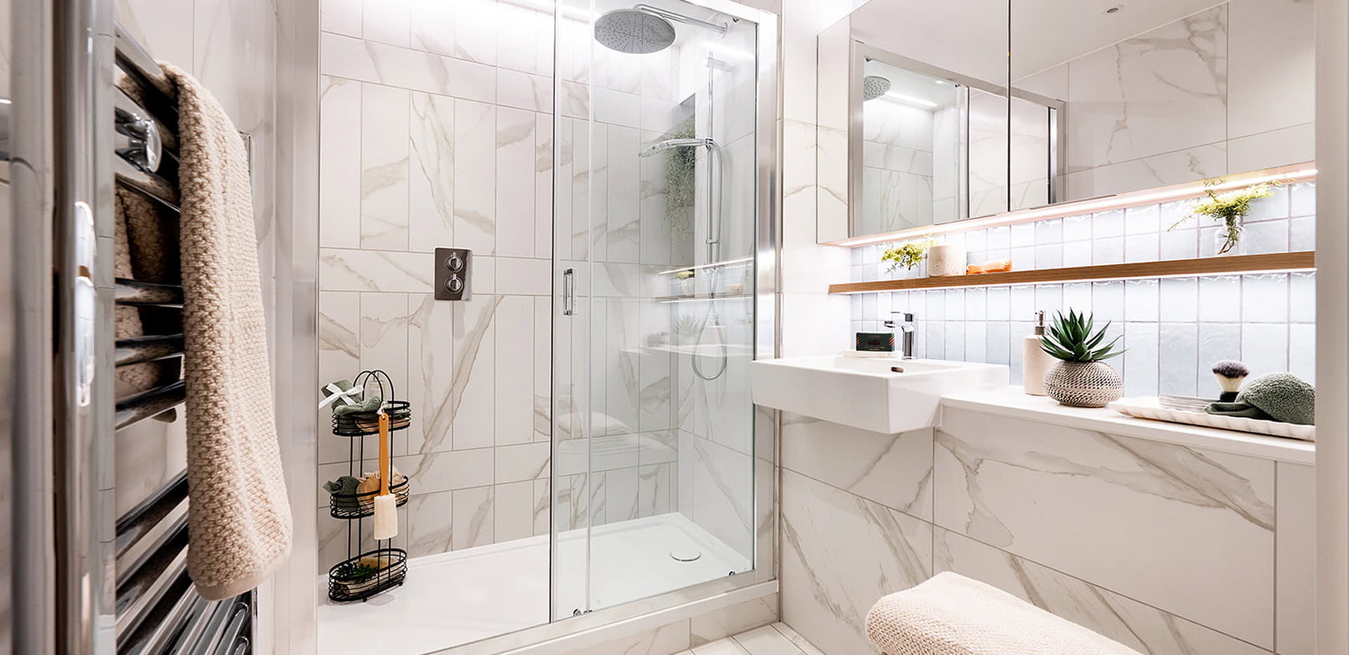 Shower unit, white and grey marble texture tiles,  wash basin with mirror above and shelving space, heated towel rack.