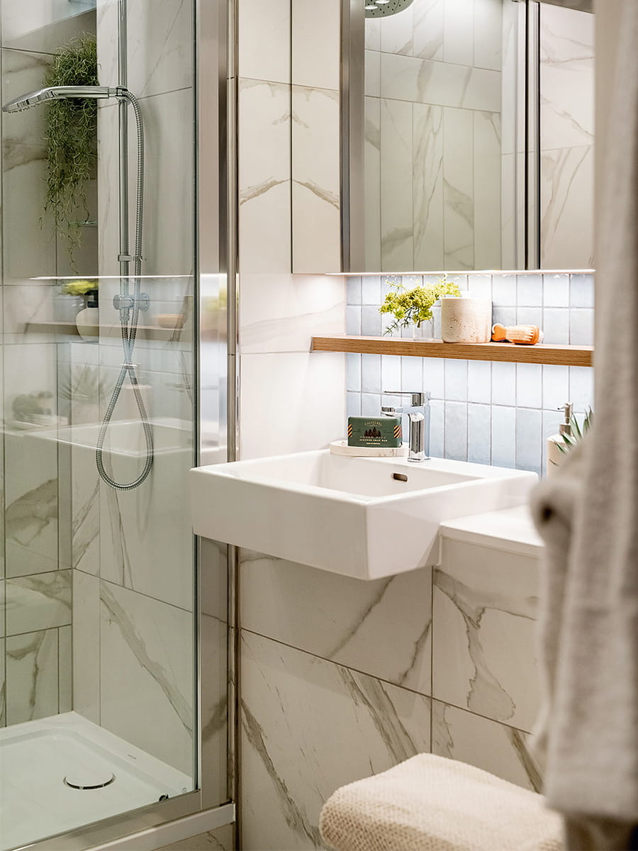 Shower unit, white and grey marble texture tiles,  wash basin with mirror above and shelving space.