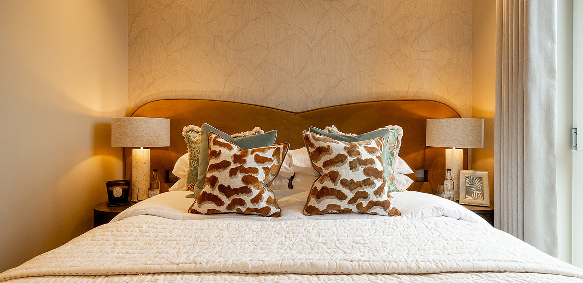 Closeup of made-up double bed, orange headboard and bedside tables.