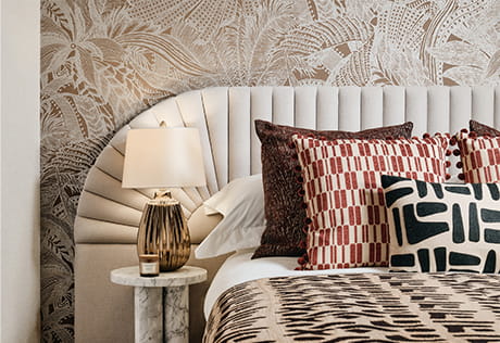 Decorated bed and cream colour headboard, with patterned wallpaper behind