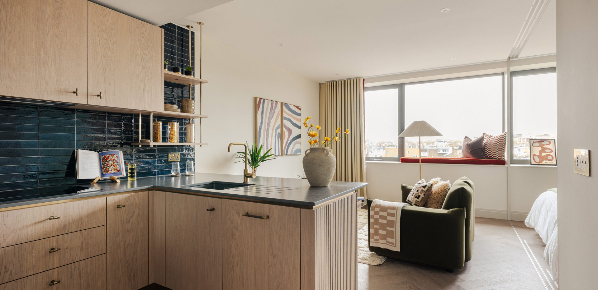 Closeup of kitchen island with dark blue-black splashback tiles, living space in background.