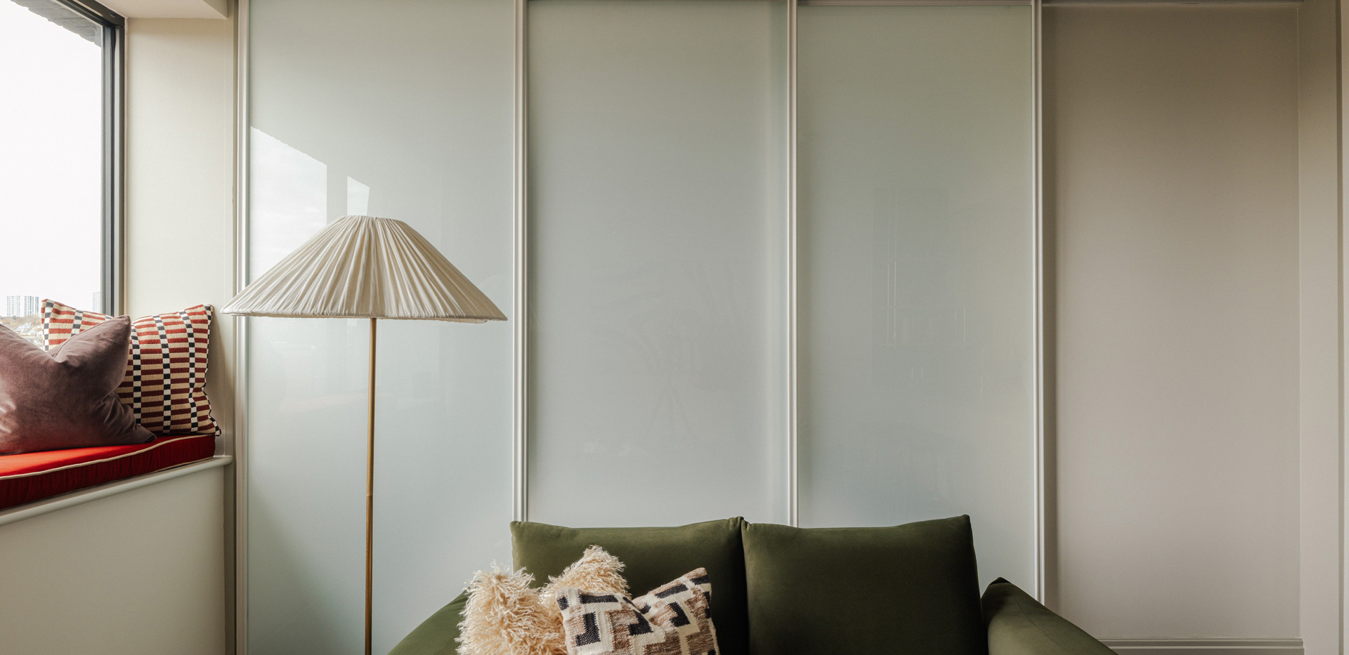 Closeup of sofa, standing light, with partition doors or wardrobe in background.