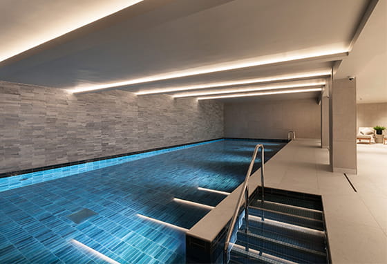 Swimming pool with stairs entry, beige grey tiled walls and warm, strip lighting above