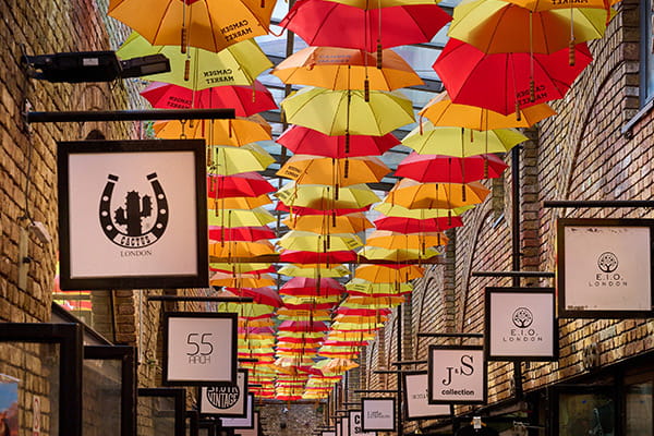 An image of shops in Camden with colourful umbrellas above the walkway