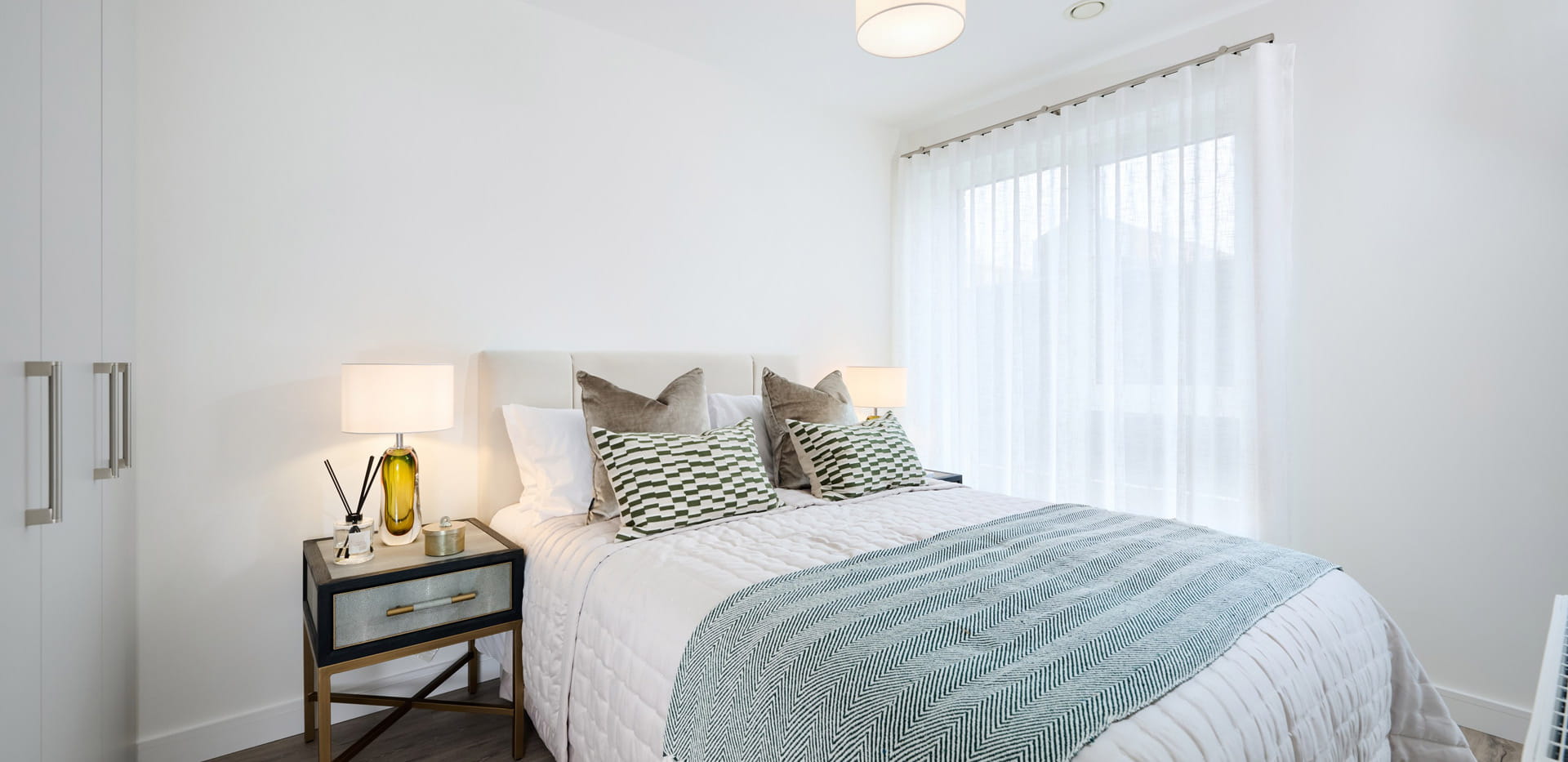 Bed and side tables, white walls, ample natural lighting from windows.