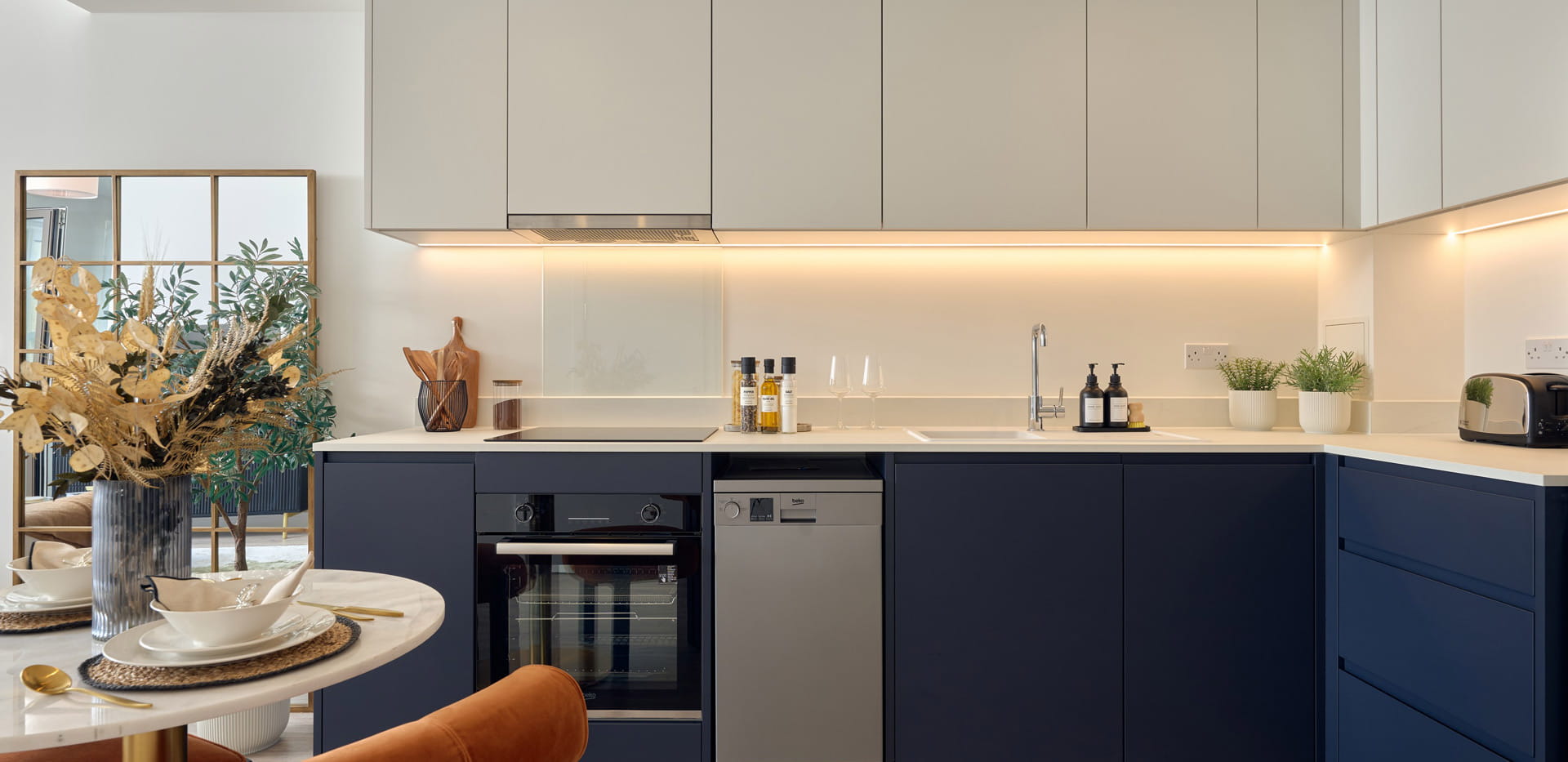 Kitchen dining space with navy blue and light grey panels, cupboards, white countertops.