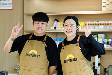 Two shopkeepers posing wearing Eggy Mart aprons.
