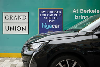 A car in the foreground, with Grand Union and Hiya Car branding on a hoarding behind.
