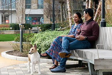 Two people sitting on a park bench with their dog.