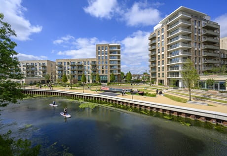 Paddle boarders on a body of water against a background of new build flats.