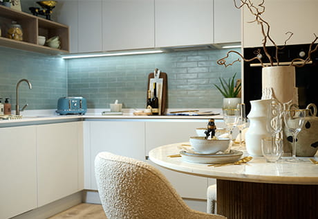 Closeup shot of circular dining table, kitchen with white cabinet surfaces and sea green splash tiles