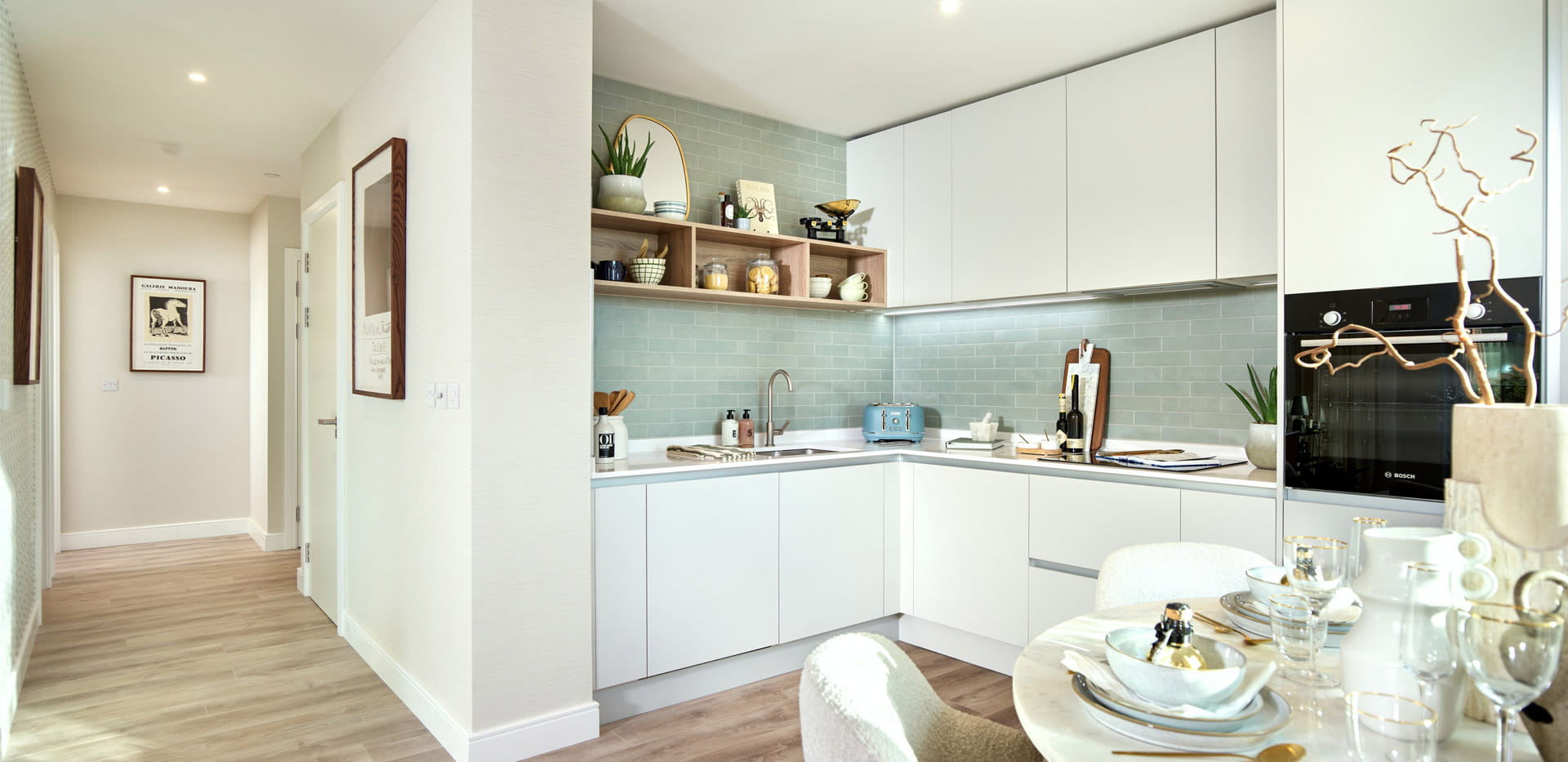 Kitchenette with white drawers and cupboard surfaces, dining table in foreground