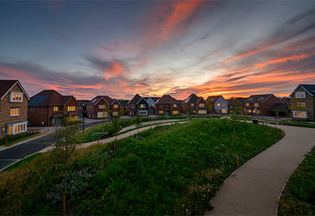 New build homes spread out along an arc, with dusk/dawn in the background and well maintained lawn in front.