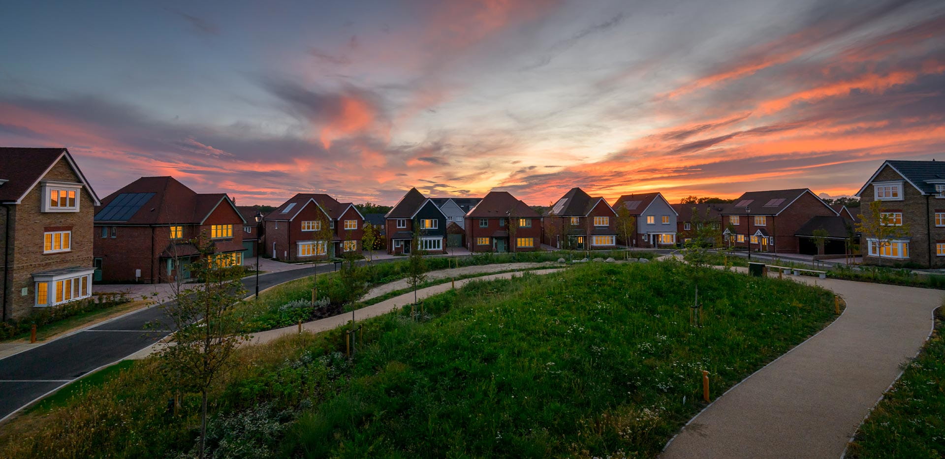 New build homes spread out along an arc, with dusk/dawn in the background and well maintained lawn in front.