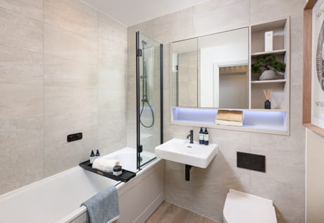 Bathroom with shower over bath, off-white tiling, wash basin with cabinet mirror, shelving.
