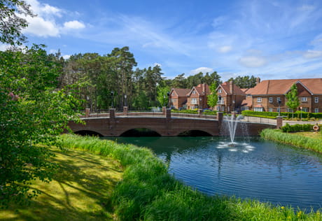 Multi-arch bridge spanning a pond with fountain, grassed areas in foreground, new development in background