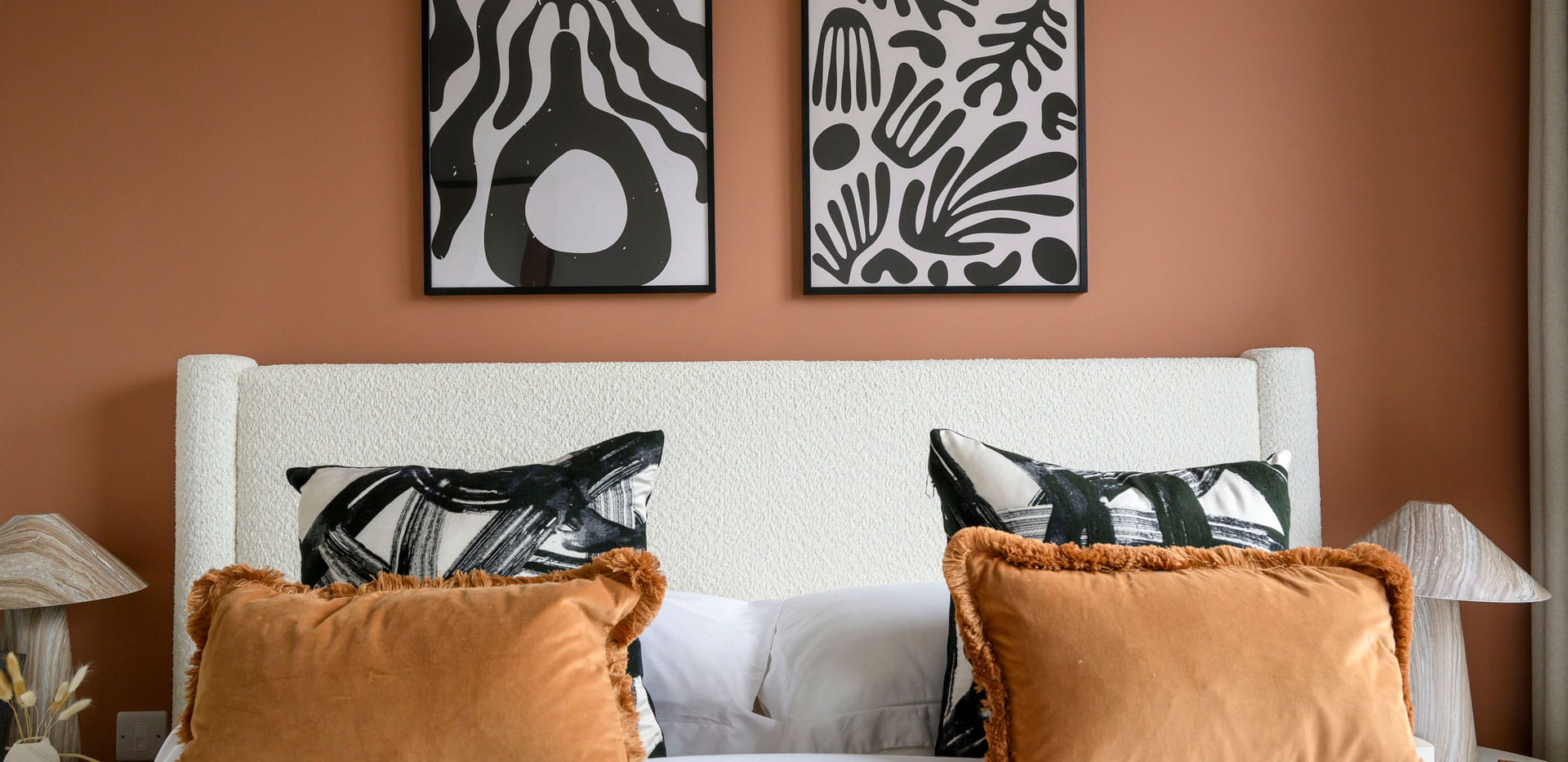 Closeup of madeup bed, cushions, wall hangings above.
