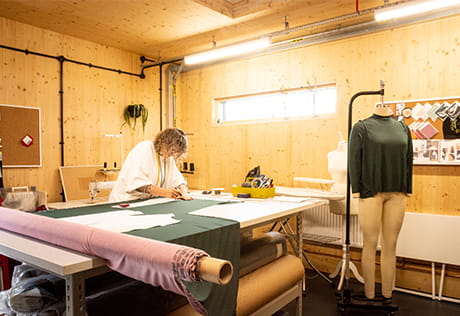 Person measuring and cutting fabric for clothing on a worktop table.