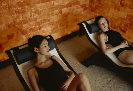 Two people relaxing on lounge chairs in a spa sauna environment.