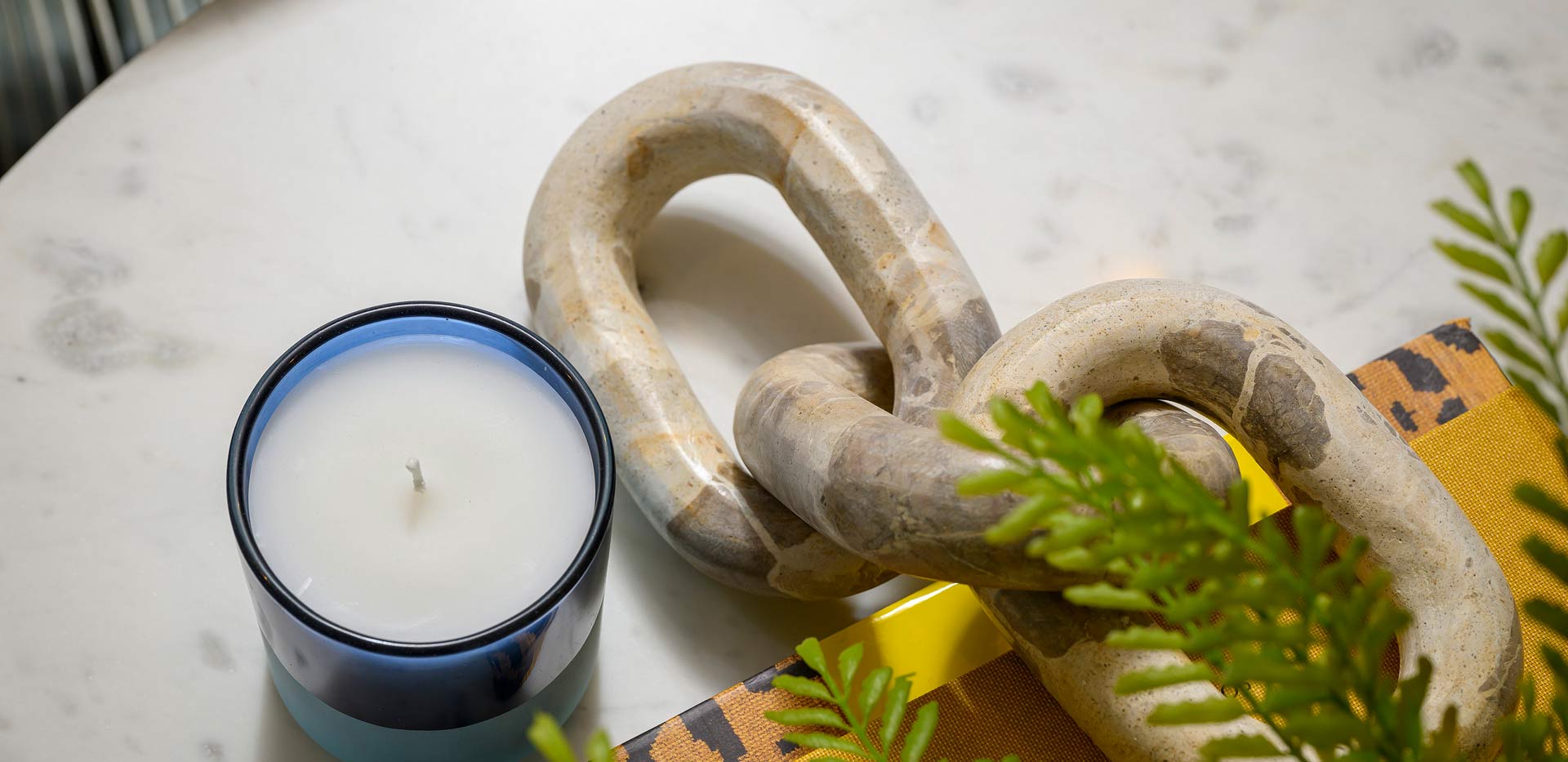 Closeup of ceramic chain, candle and fern plant on countertop