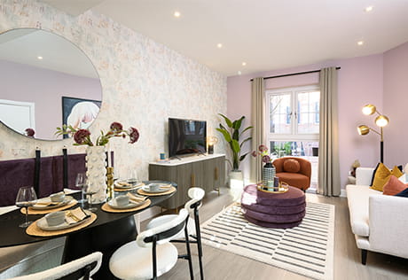 Modern open-plan living and dining room with pastel walls, set table, TV, sofa, armchair and large round mirror.