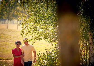 Image of a man and woman walking through a field with trees on a summer's day