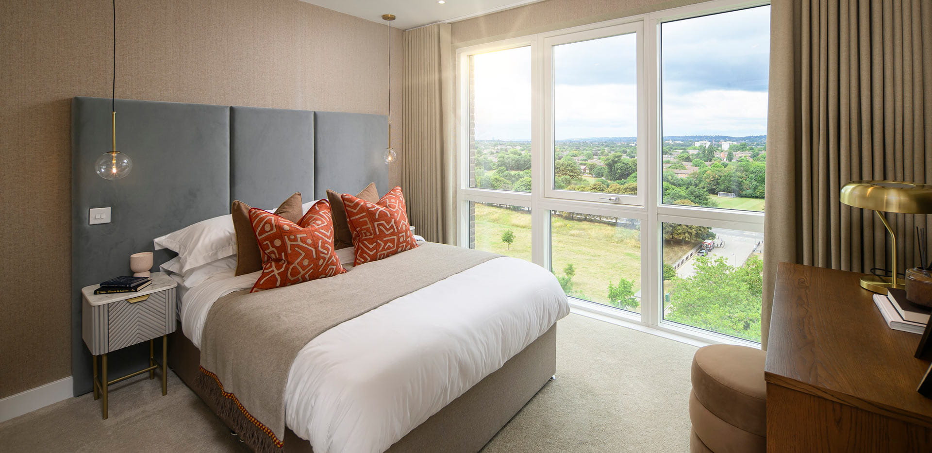 Double bed with tall fabric headboard, bedside tables and wall hanging, desk table and ample natural lighting from multiple windows.