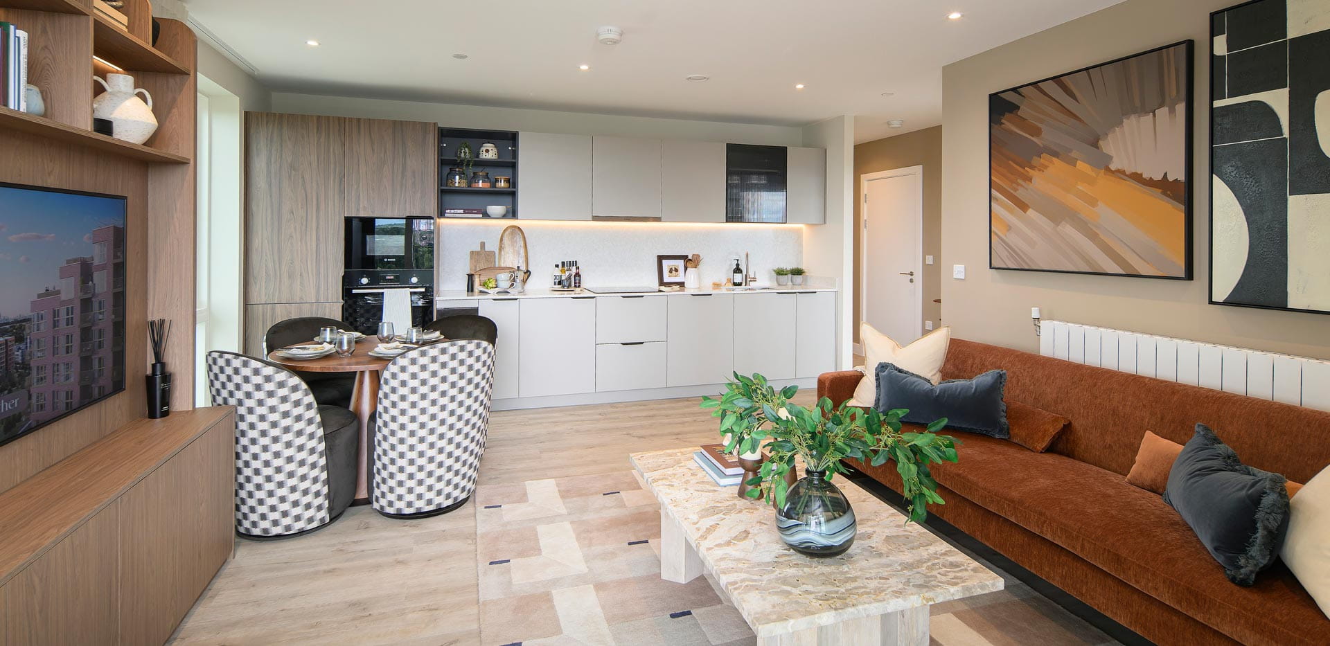 Living space with TV shelving unit, stone coffee table and fabric sofa, kitchen in background.