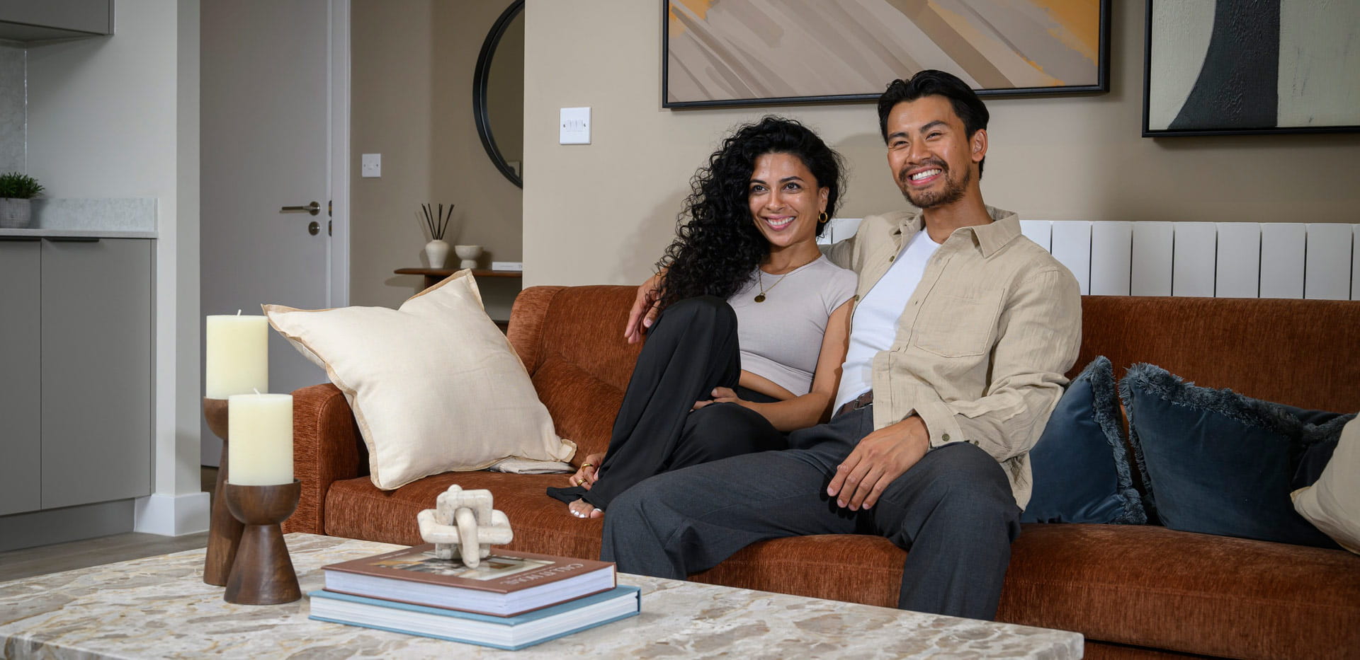 Male and female reclining on sofa smiling, showcasing living space of new build apartment.