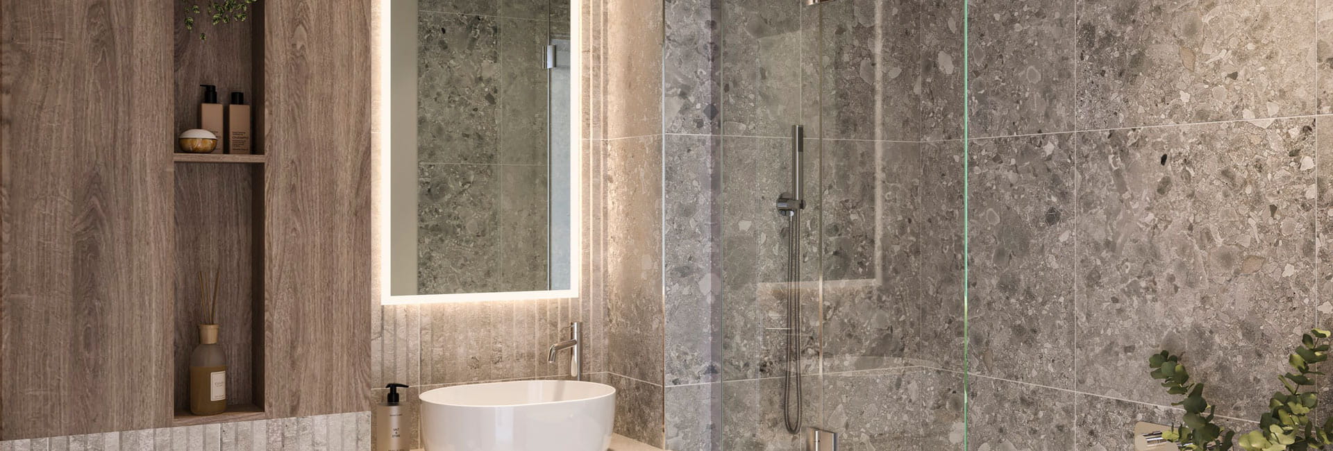 Shower over bath, spotted grey tiling effect, wash basin with vanity lighting around mirror, shelving unit.