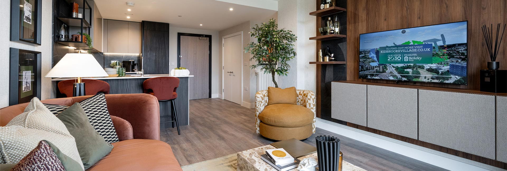 Modern designed living space with sofa coffee table, TV unit, kitchen dining area in background.