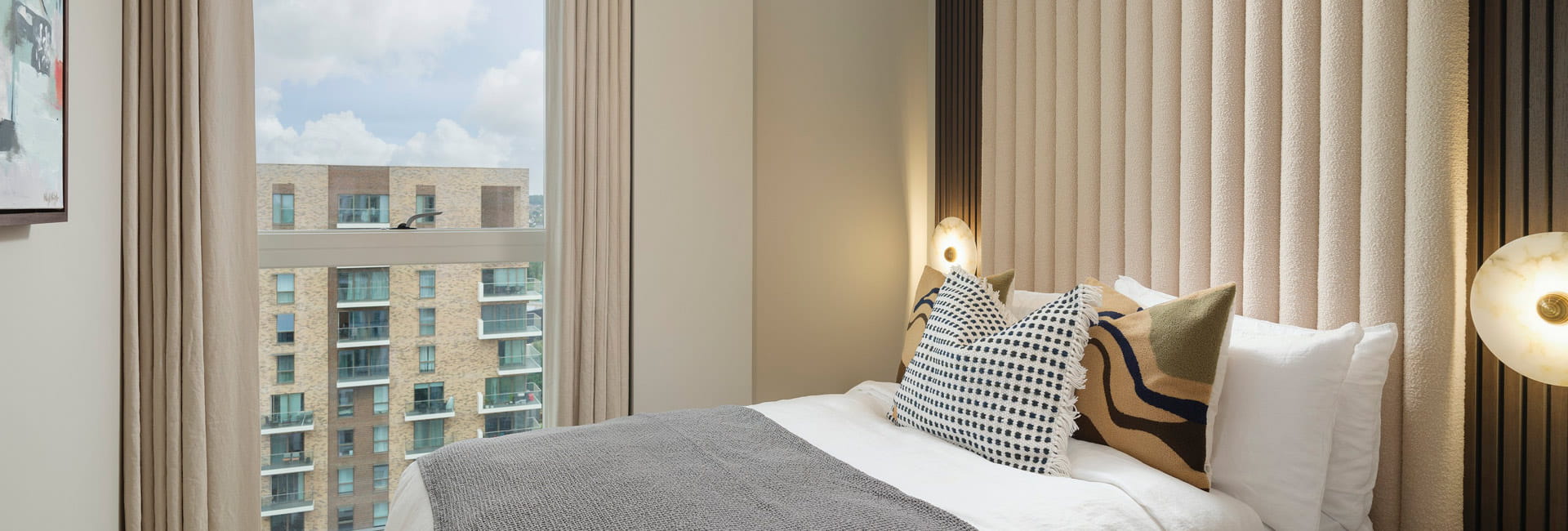 Made-up bed with wide, velvet headboard, floor to ceiling curtains.