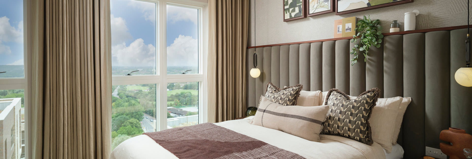 Made-up bed with wide, velvet headboard, floor to ceiling curtains.
