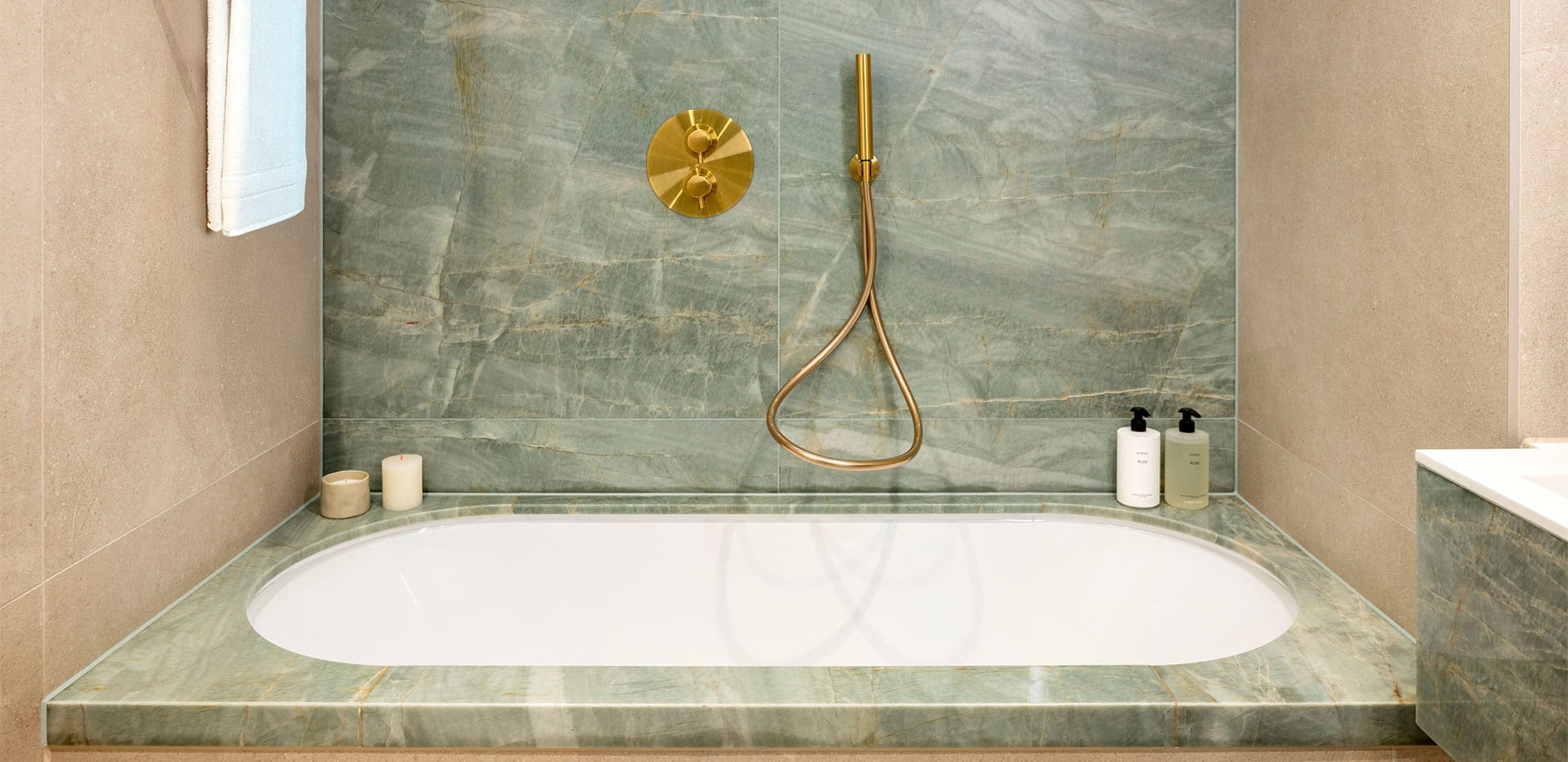 Bathtub with marble pattern decorated rim, gold colour taps and shower head, marble and beige walls
