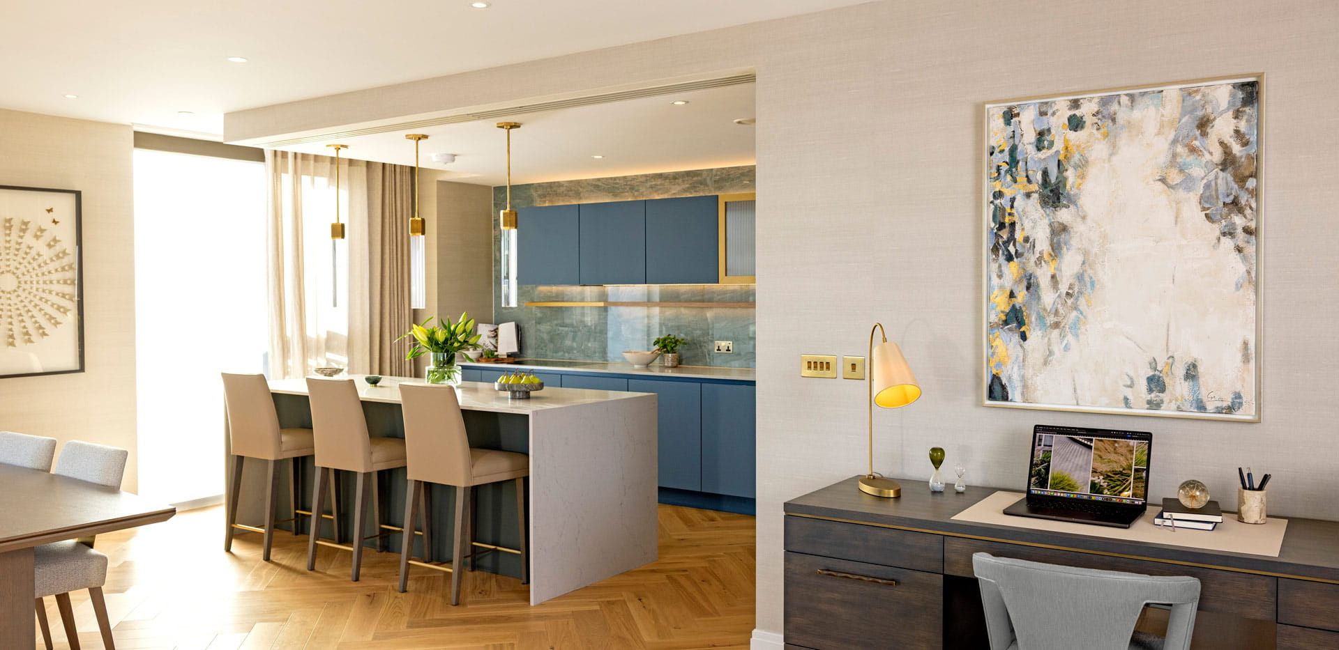 Desk with wall hanging in foreground, partial view of dining table and kitchen and kitchen-breakfast island in background