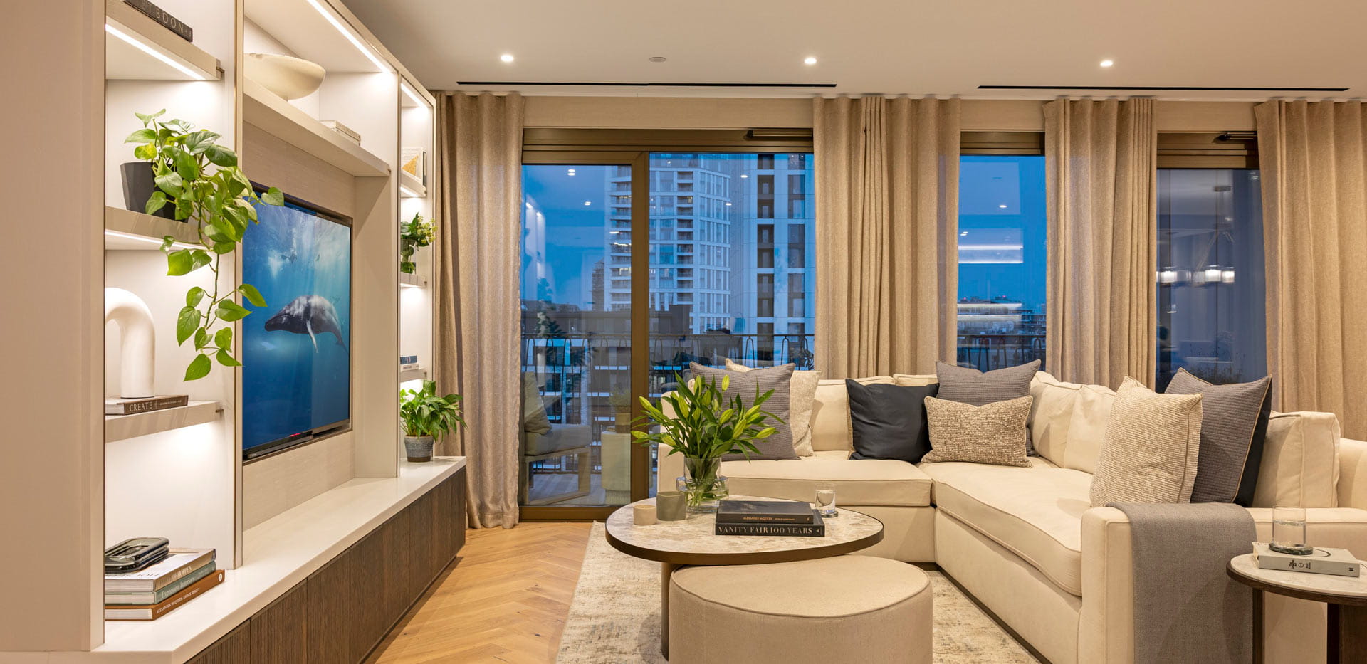 Living space with L-shaped sofa, round coffee table, wall mounted TV inside wall shelving unit