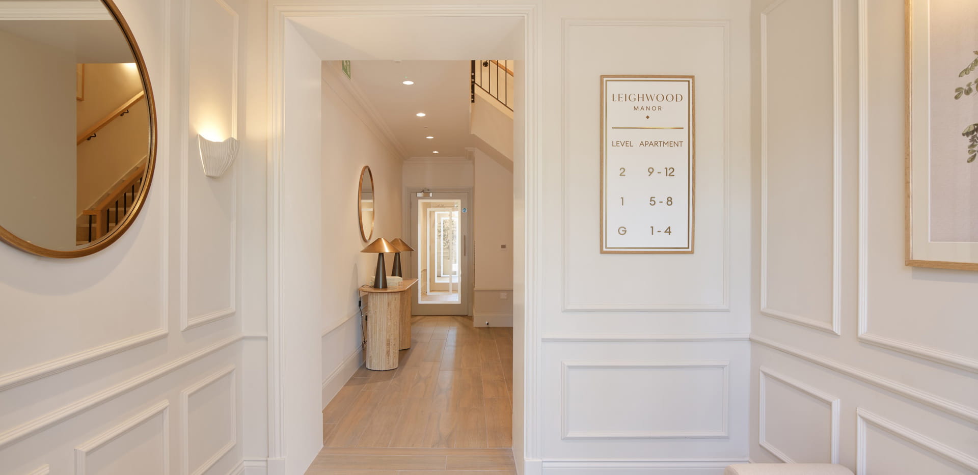 Hallway with panel walls, wall hangings, wood flooring.