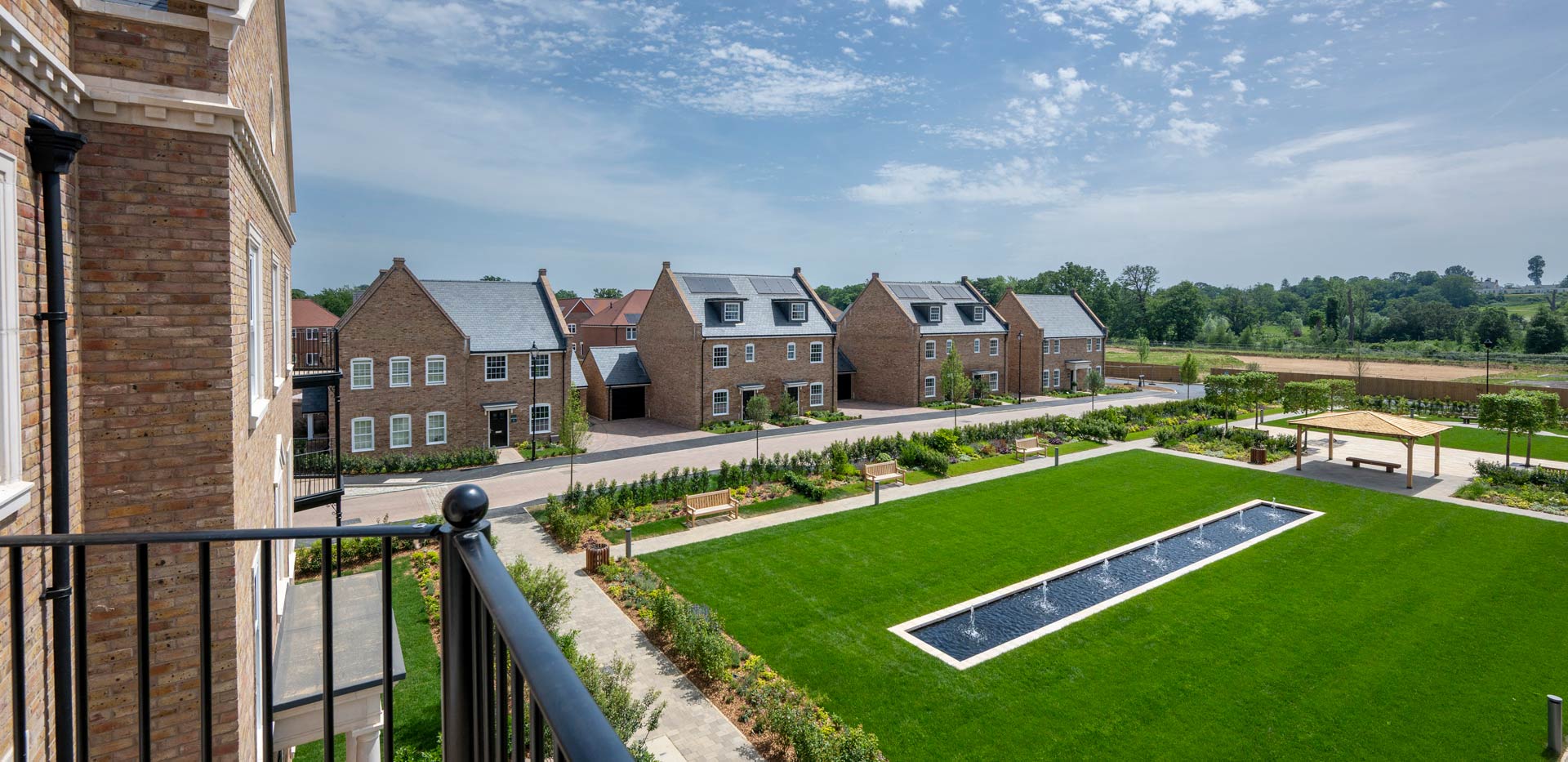 CGI of external development housing facades from above, central water feature and mowed lawns below.
