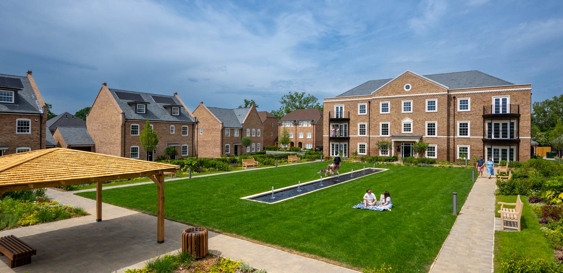 CGI of external development housing facades, central water feature amongst mowed lawns.