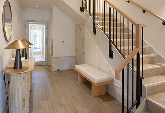 hallway of interior home, wall table, ottoman style seating, cupboard under stairs.