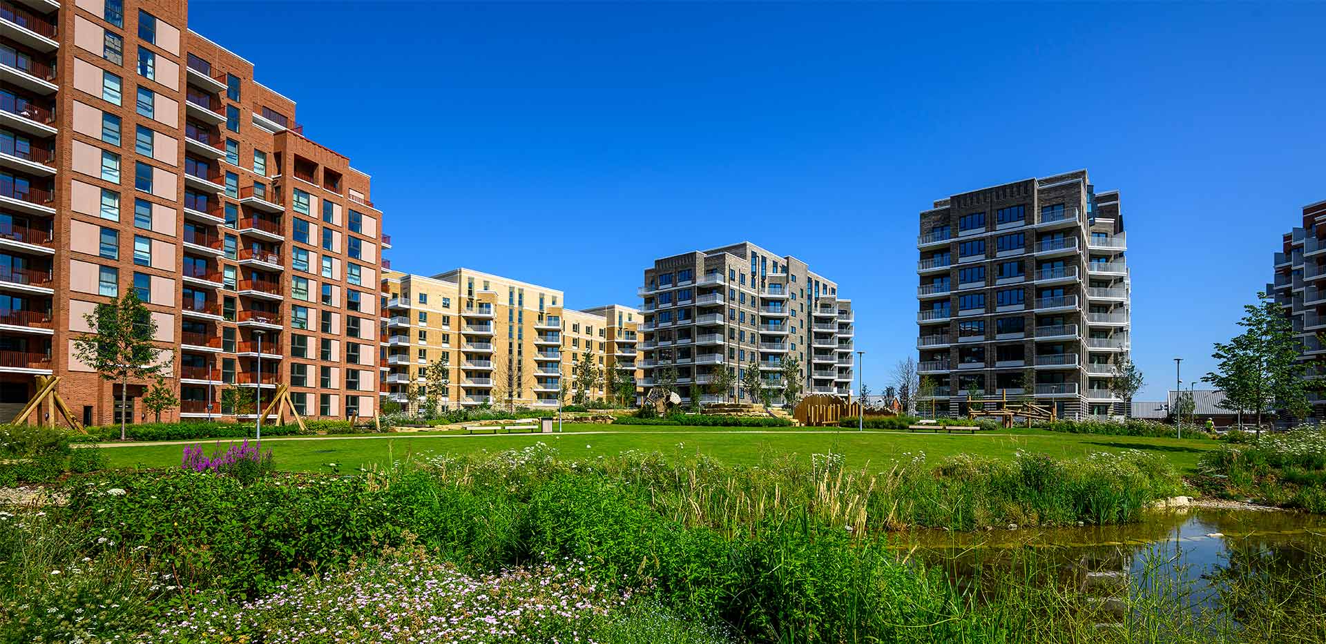 CGI of new build block of flats in background with landscaped greenery and water body in foreground.