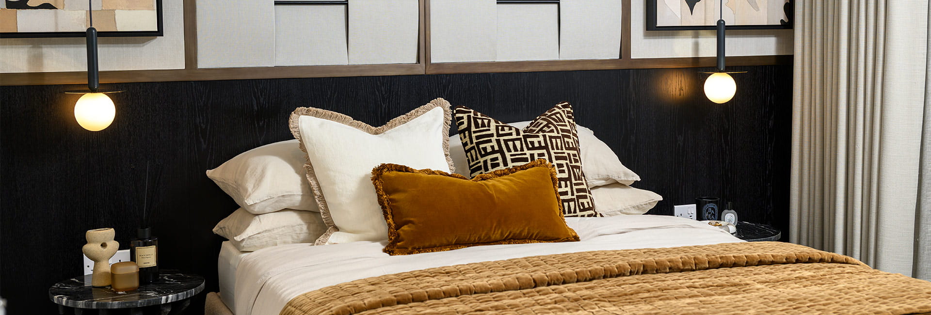 Modern bedroom with a neatly made bed, patterned cushions, bedside tables, pendant lights and wall art