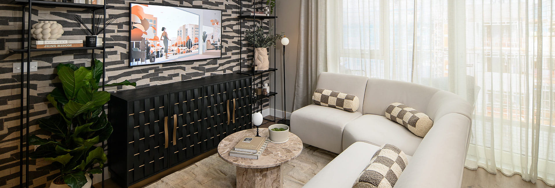 Modern living room with cream sofas, round marble table, patterned feature wall and floor-to-ceiling curtains.