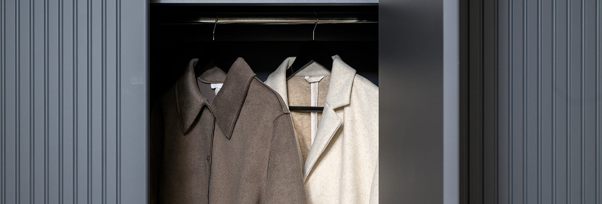 Partly open dark wardrobe with beige and cream coats hanging inside.