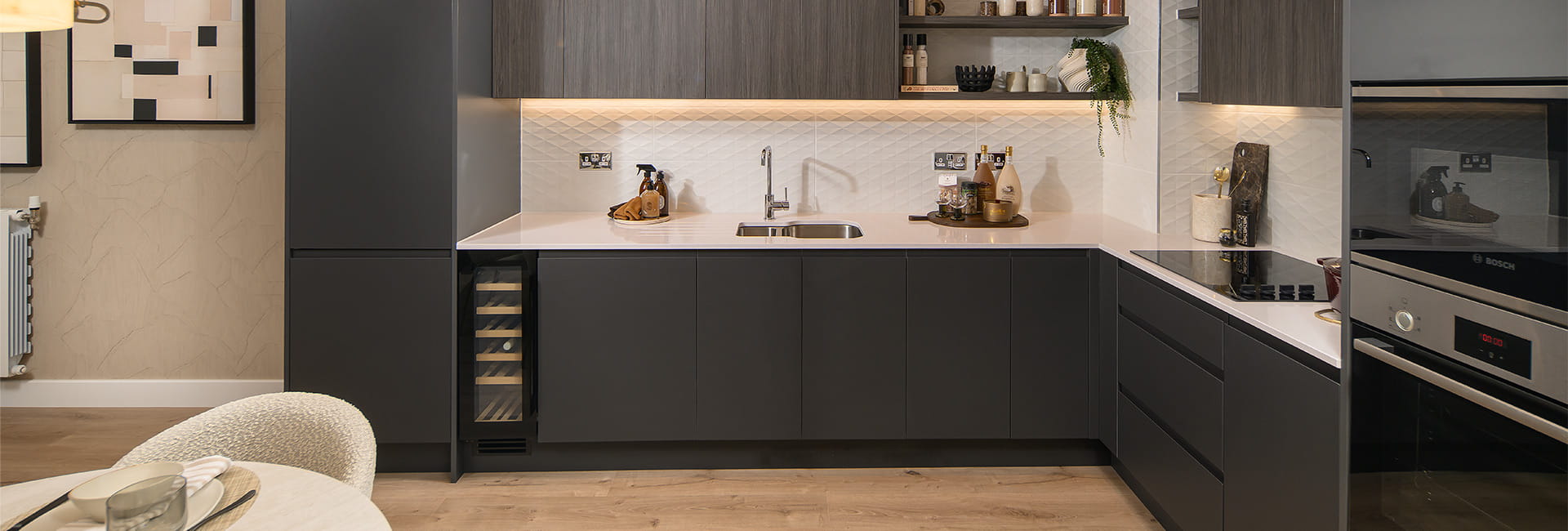 Modern open-plan kitchen with dark cabinets, white worktops, integrated appliances and wooden flooring.