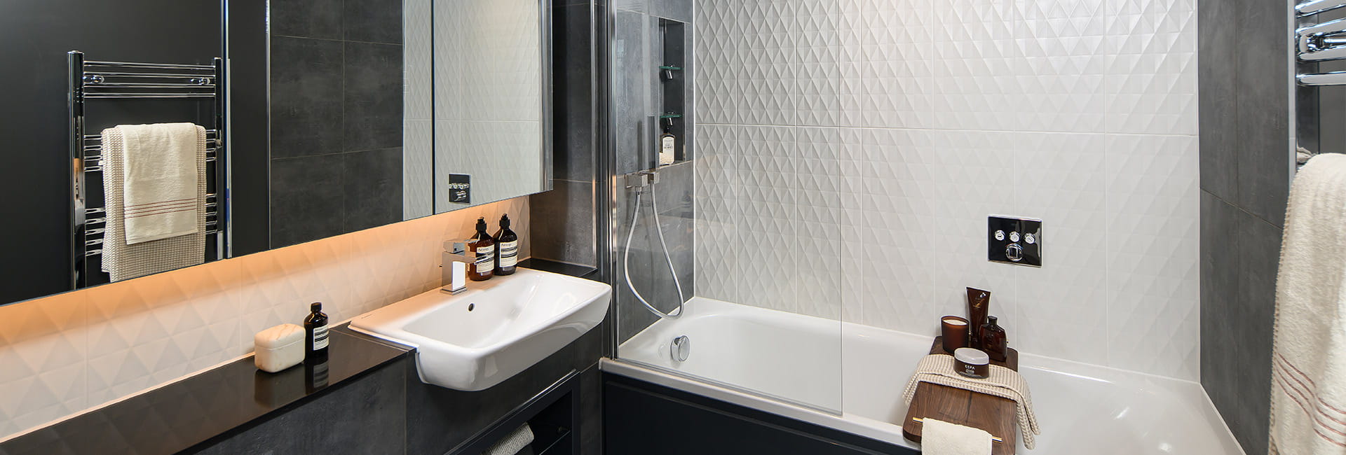 Modern bathroom with a sink, mirrored cabinet, bath with shower screen, and dark grey and white tiles.