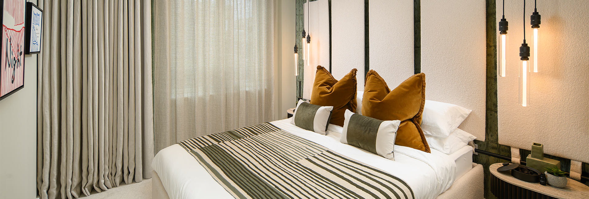 Modern bedroom with a neatly made double bed, striped throw, tall curtains and hanging bedside lights.