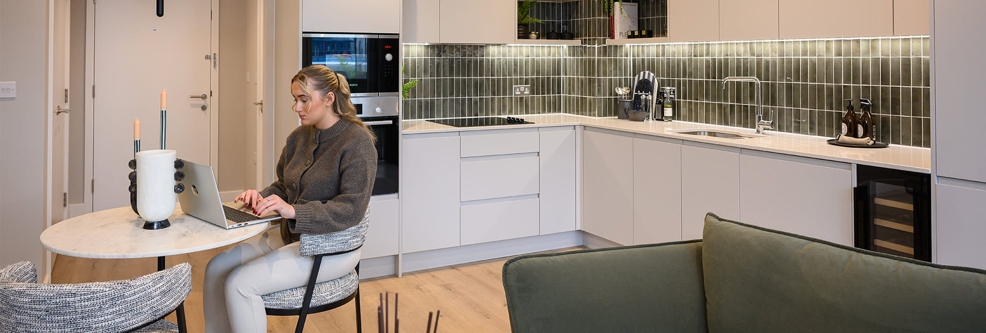 Woman working on a laptop at a round table in a modern open-plan kitchen and living area.