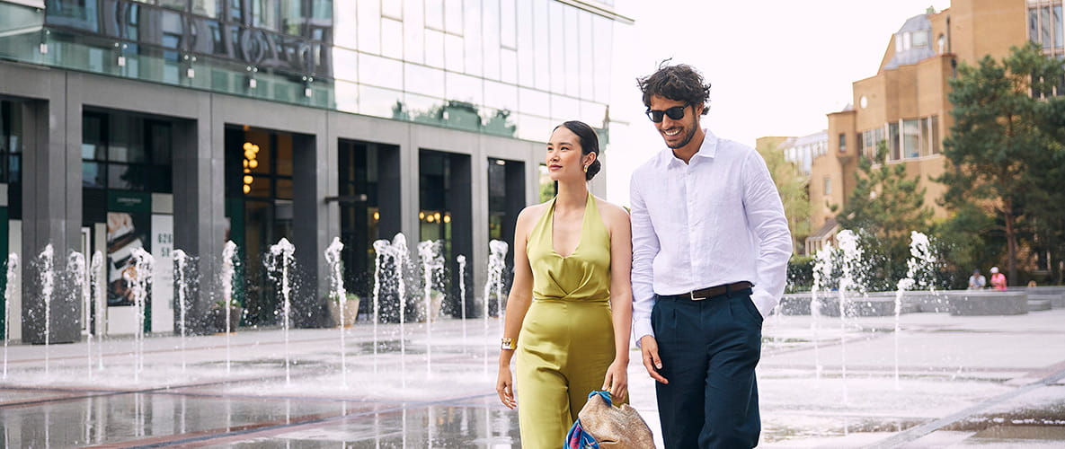 A smartly dressed couple walking near the fountains at London Dock